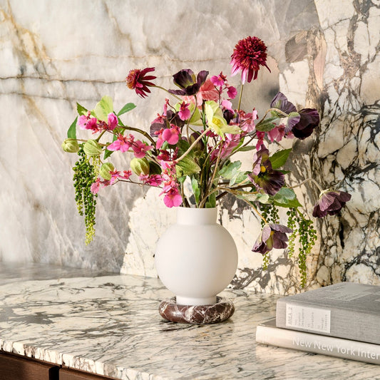 White vase with pink and purple flowers on a marble surface